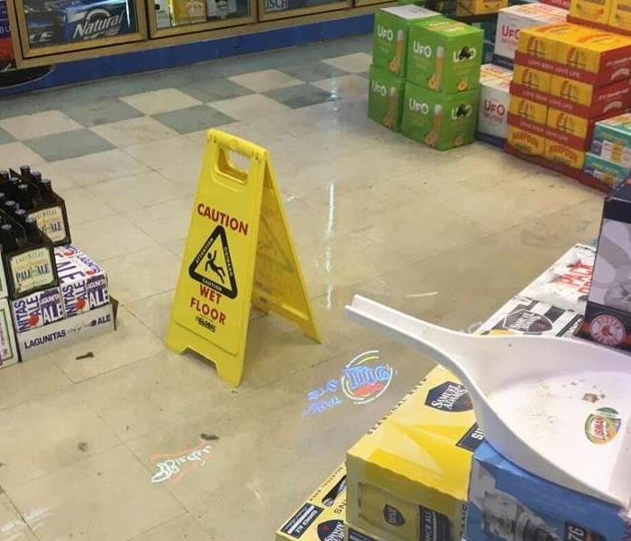 Wet floor sign in standing water on floor in liquor store with cases of beer surrounding water