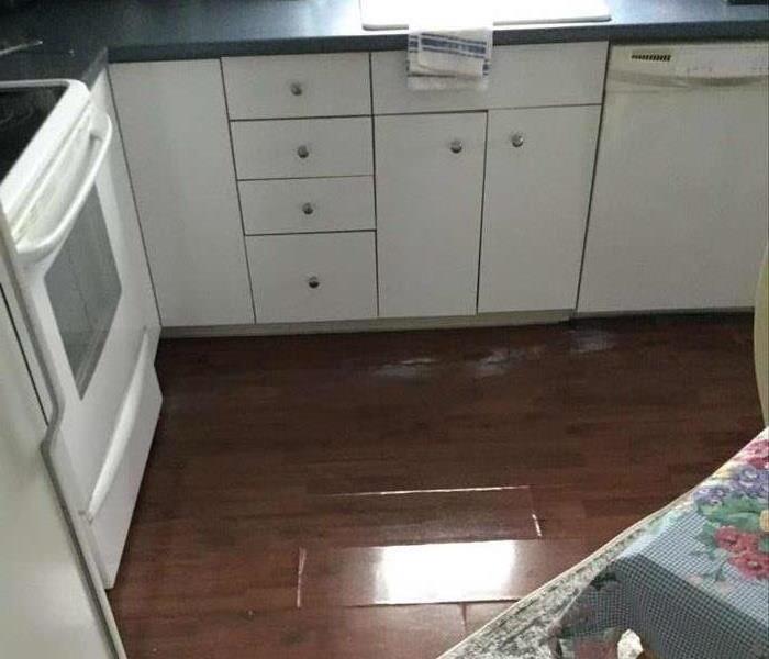 Standing water in kitchen next to white kitchen cabinets, oven and sink