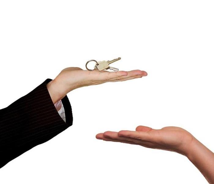 the arm of a person in a suit with keys in their outstretched hand over another outstretch hand ready to receive them
